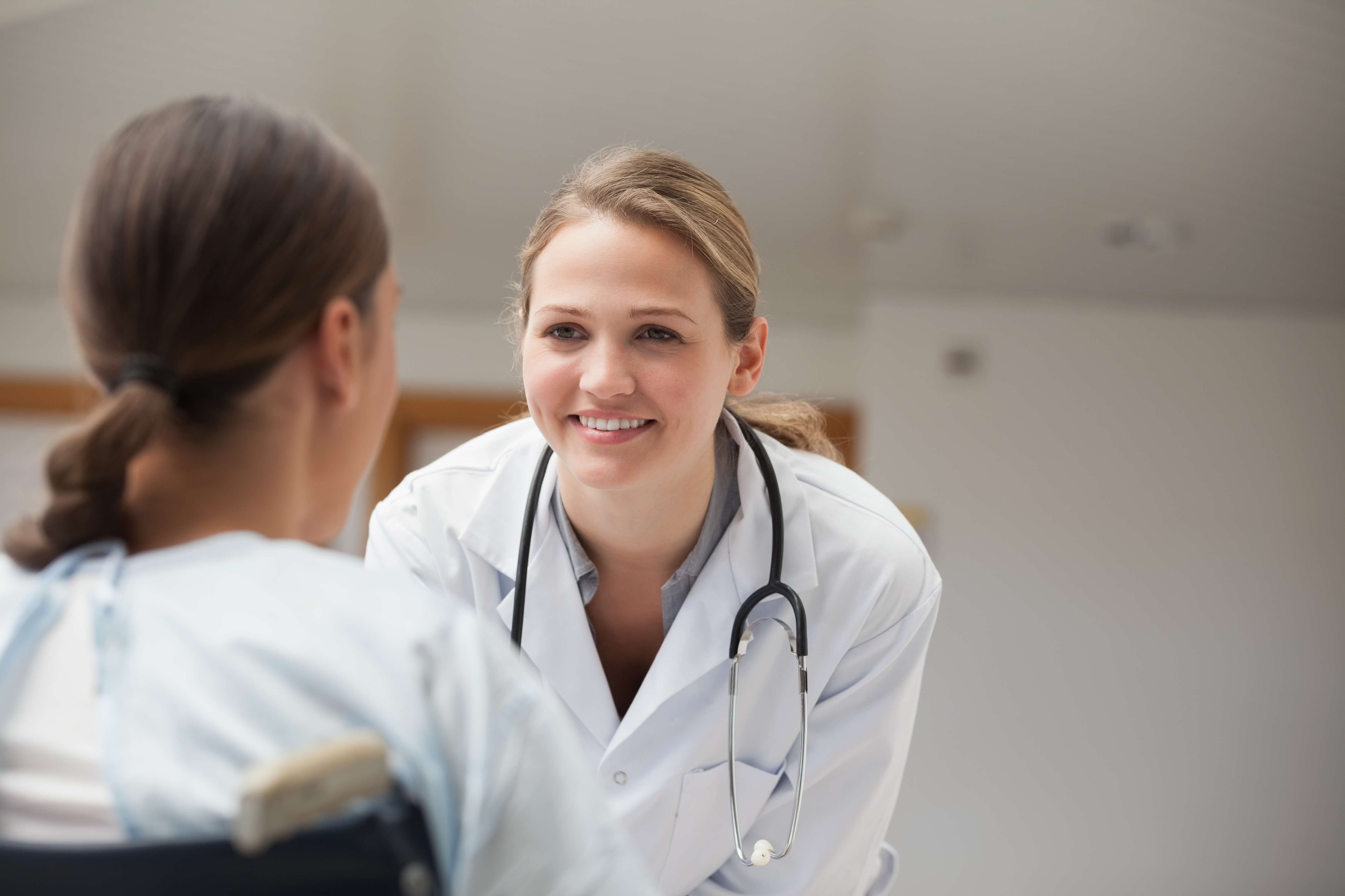 Smiling doctor looking at a patient on a wheelchair in hospital hallwa